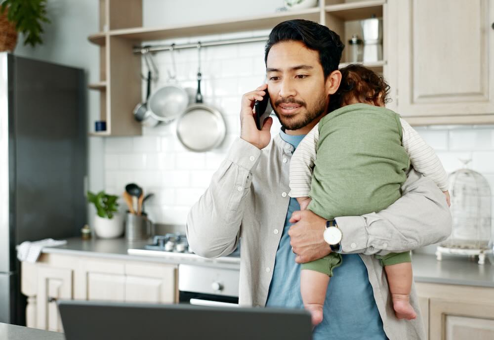 Man talking on a phone holding a baby 